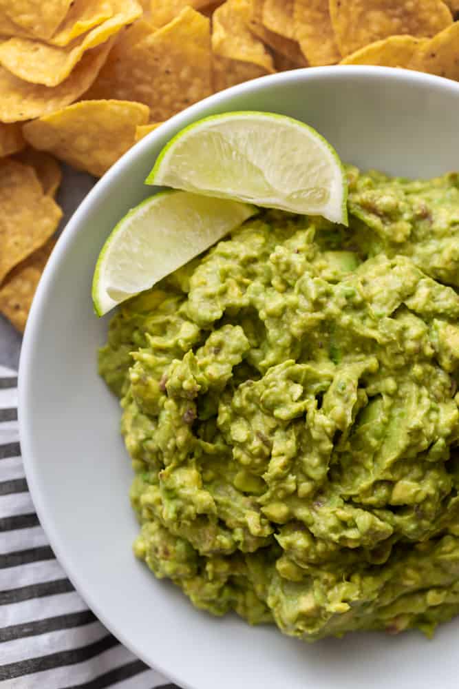 guacamole in a white bowl with two slices of lime.