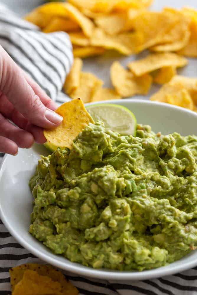 Hand dipping tortilla chip into guacamole