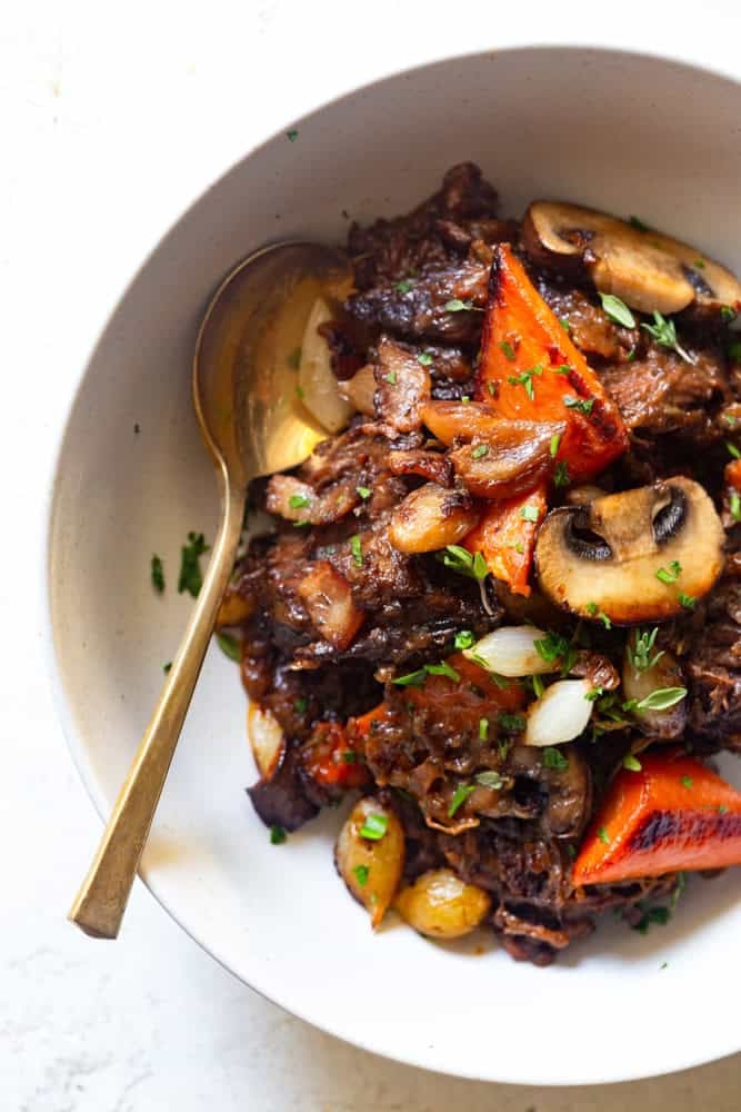 Red wine beef stew with caramelized mushrooms, carrots and peal onions in a white bowl.