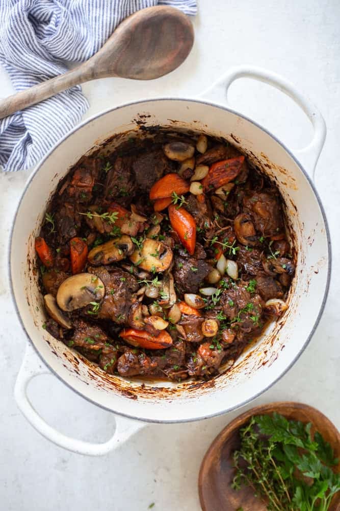 Finished red wine beef stew with caramelized carrots, mushrooms and pearl onions, garnished with fresh herbs.