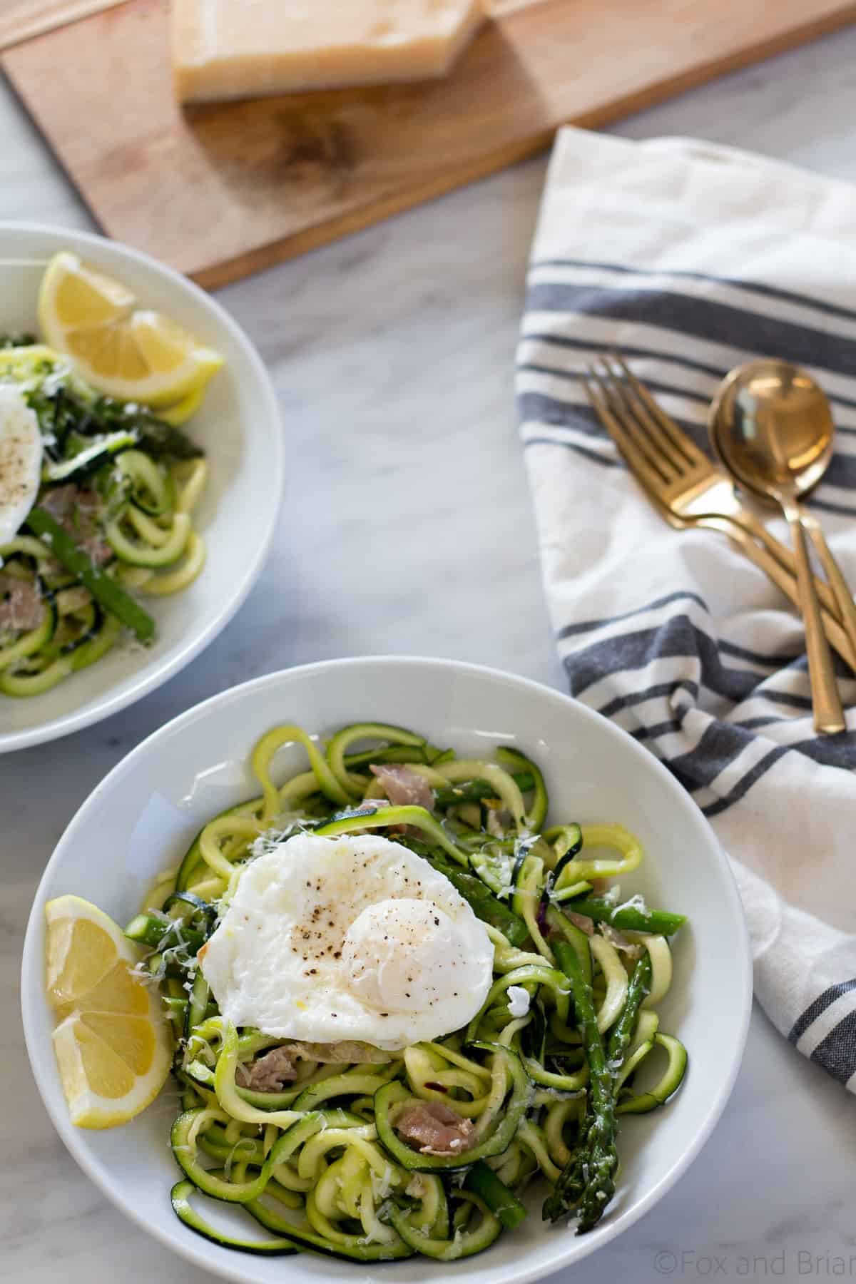 Zoodles (zuchinni noodles) quick cooked with asparagus, prosciutto, parmesan cheese, lemon and white wine all topped with a poached egg make a quick and light spring meal.