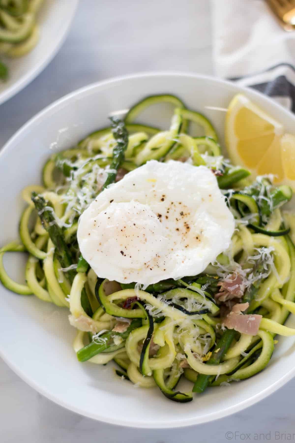 Zoodles (zuchinni noodles) quick cooked with asparagus, prosciutto, parmesan cheese, lemon and white wine all topped with a poached egg make a quick and light spring meal.