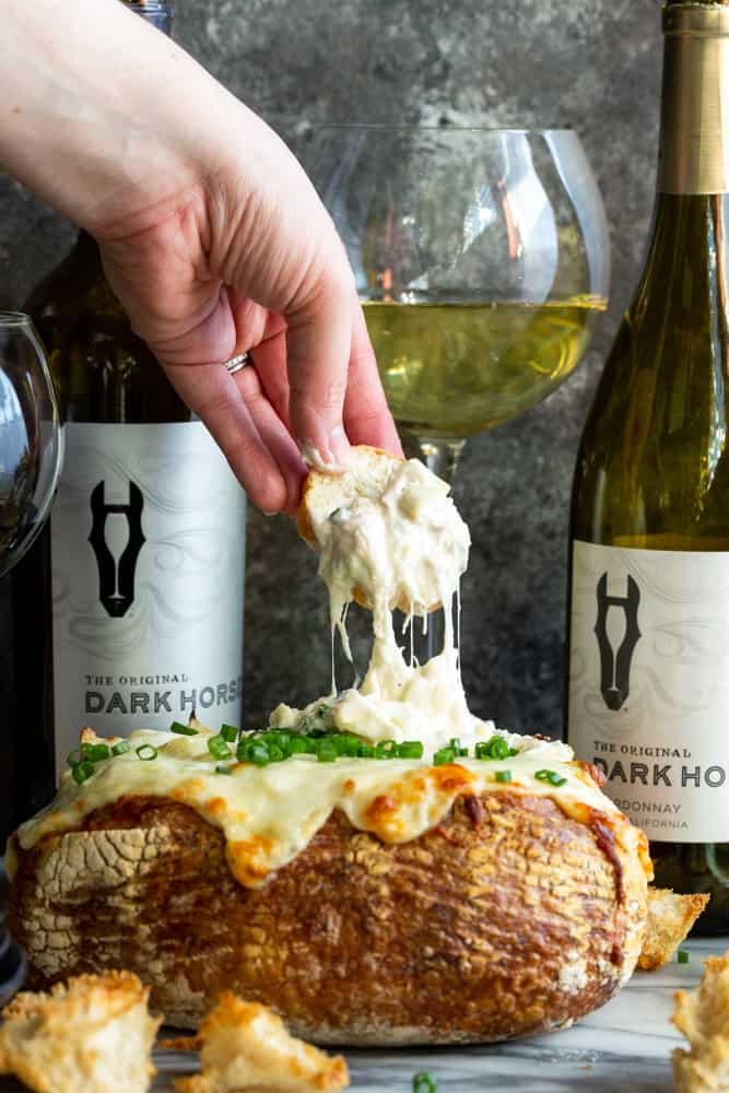 #ad This creamy and cheesy Baked Crab Artichoke Dip in a Bread Bowl will be a hit on game day! A little @darkhorsewine Chardonnay in the dip adds a complex flavor for a winning appetizer. | Dip recipe | party appetizers | crab recipes | Crab artichoke dip | Dip in a bread bowl
