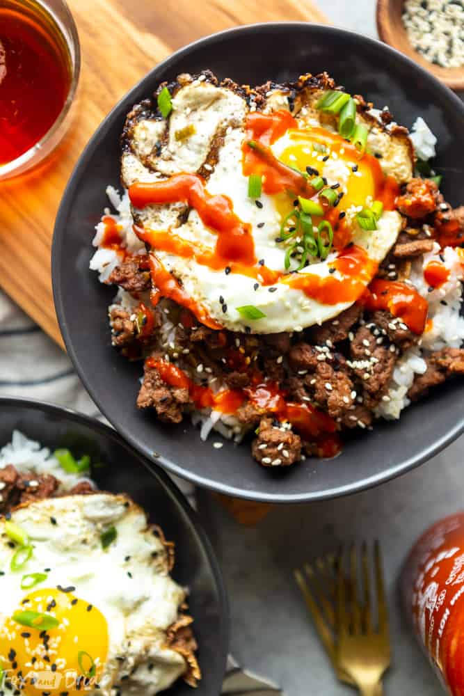 Korean ground beef bowl with a fried egg on top, drizzled with sriracha.