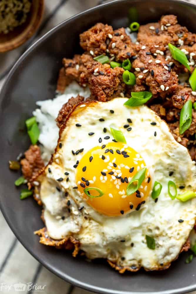 Fried egg garnished with black sesame seeds, on top of Korean Ground Beef and rice in a bowl.