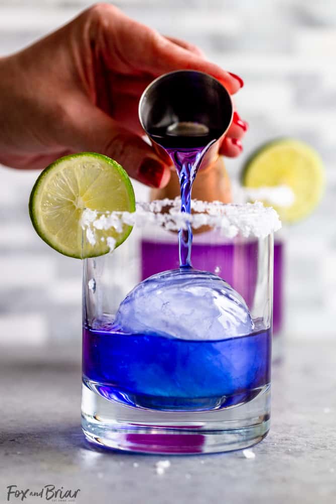 pouring blue tequila into a glass with ice