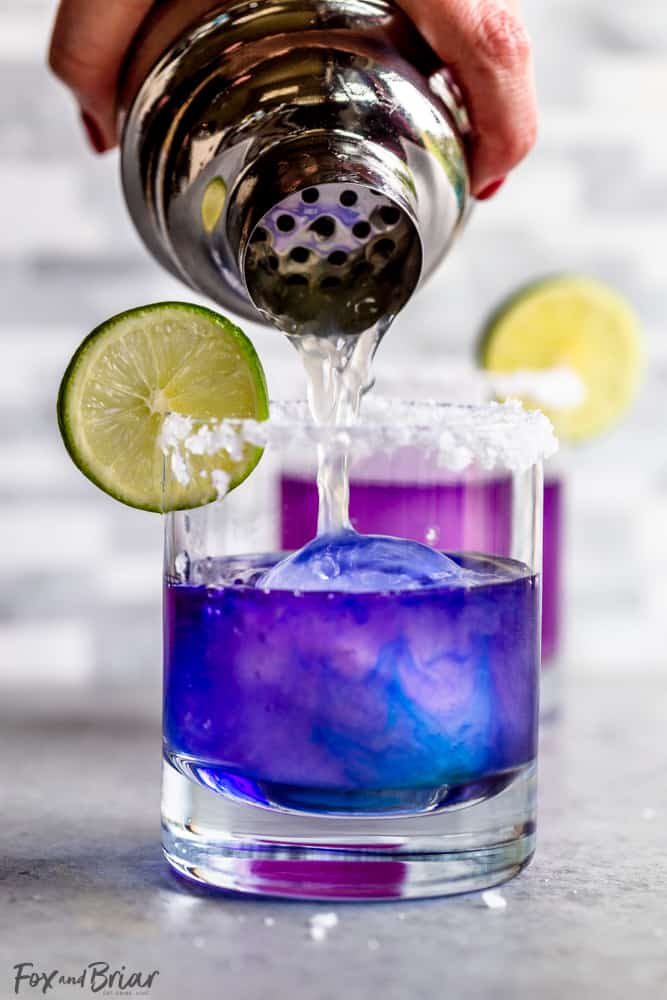 Cocktail shaker pouring lime juice into blue margarita as it turns purple