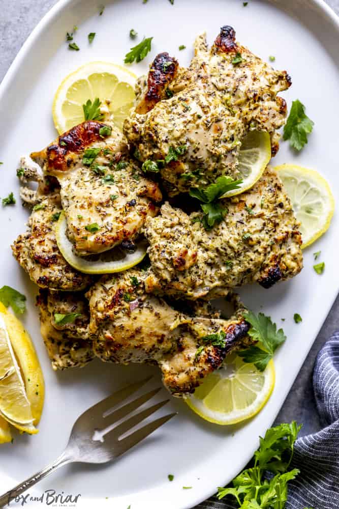 Roasted chicken thighs on a white plate with lemon slices