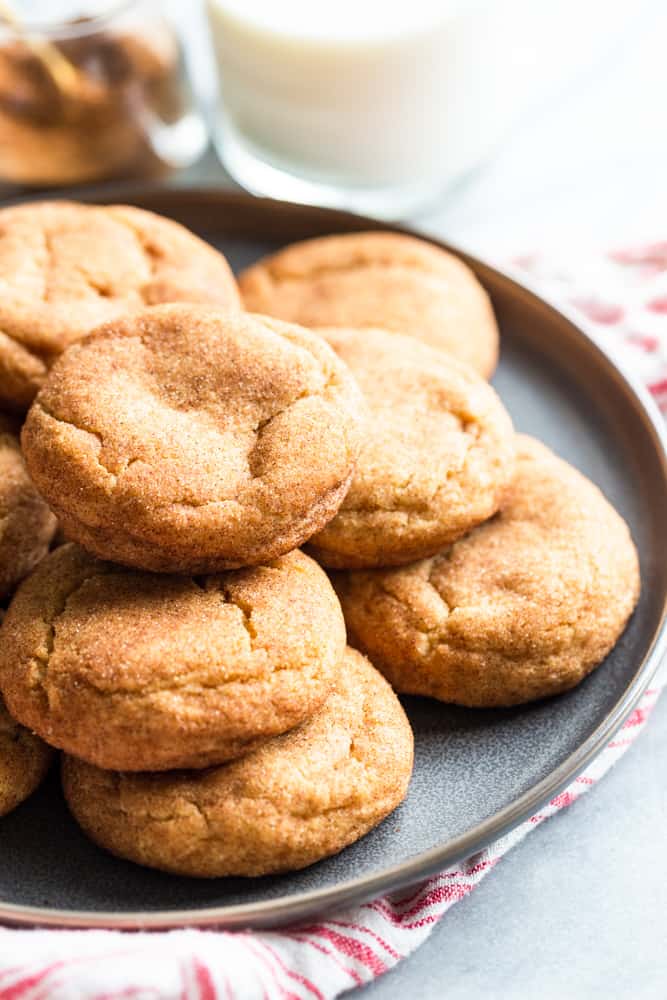 A pile of sinickerdoodles on a plate next to a glass of milk