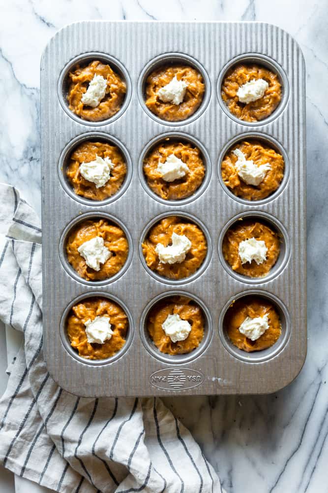 Pumpkin muffin batter with cream cheese dollops on top before baking