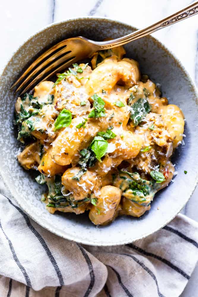 Bowl of Gnocchi with kale and sausage in creamy pumpkin sauce with a fork.
