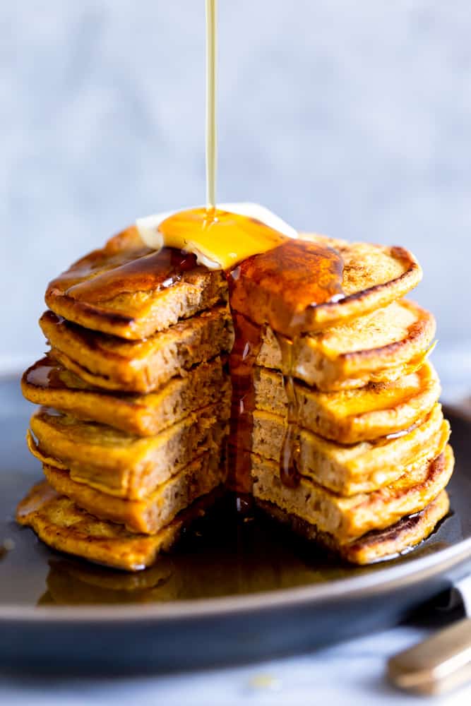 Syrup pouring onto a stack of pumpkin pancakes with a wedge cut out.