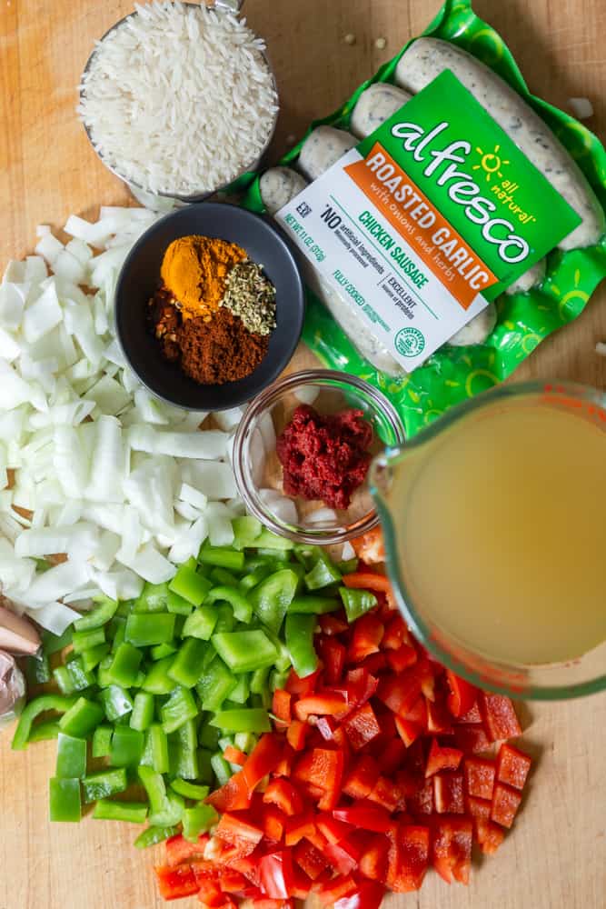 chopped peppers and onions, chicken stock, rice, spices, tomato paste and chicken sausage on cutting board