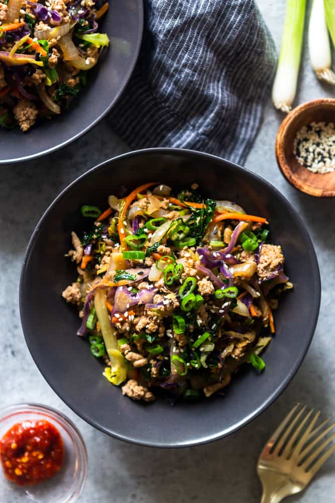 finaly egg roll in a bowl recipe plated on black bowls, with sides of sesame seeds, green onion and chili garlic sauce