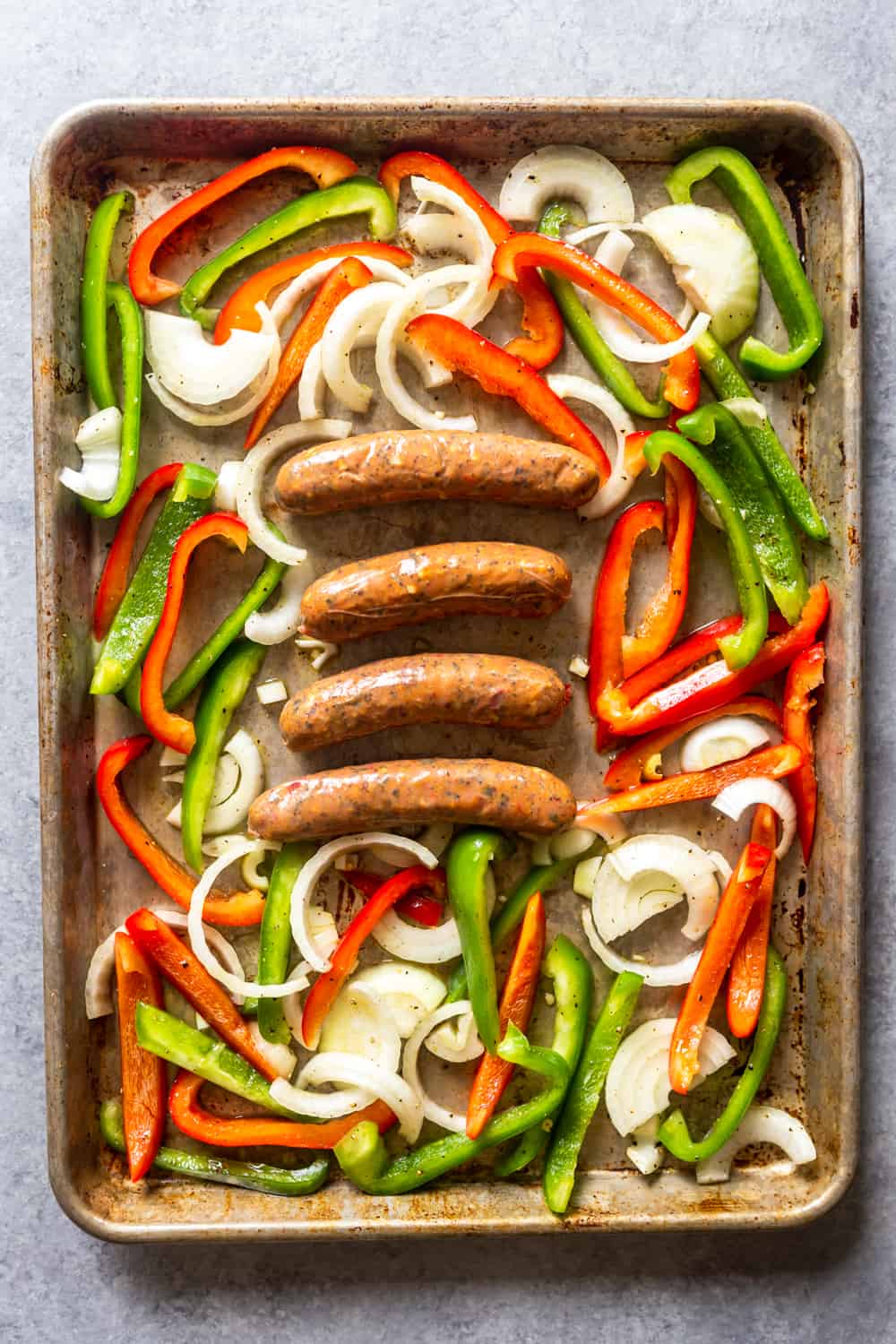 Raw peppers, onions and sausages on a sheet pan before going into the oven.