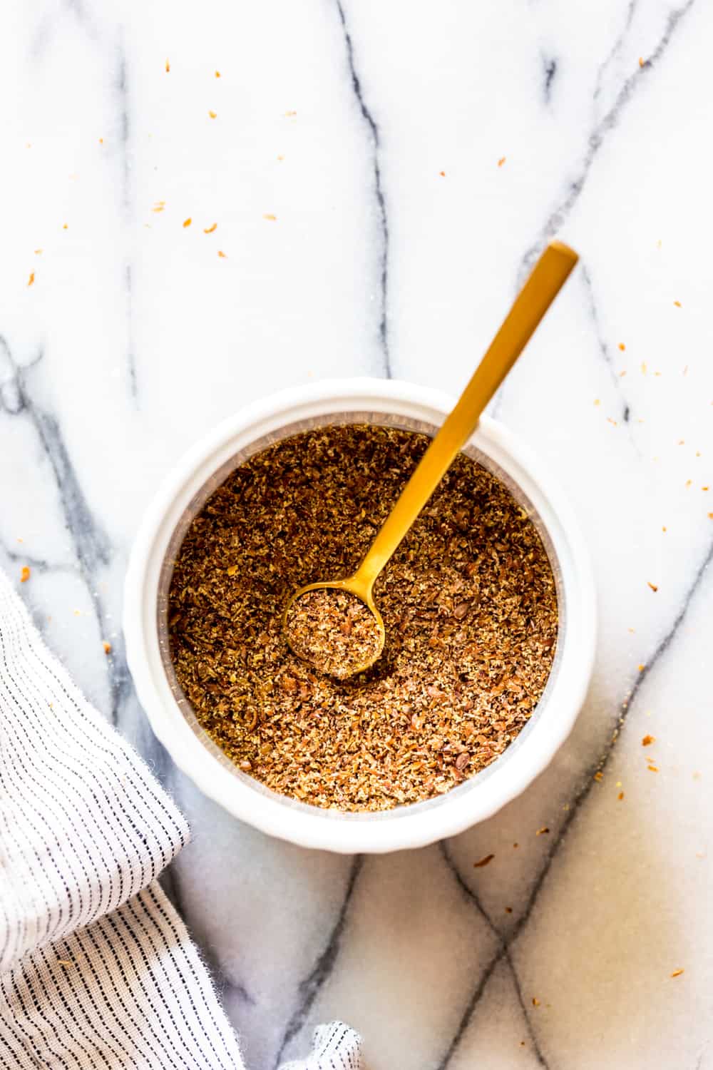 ground flax in a white bowl with a gold spoon