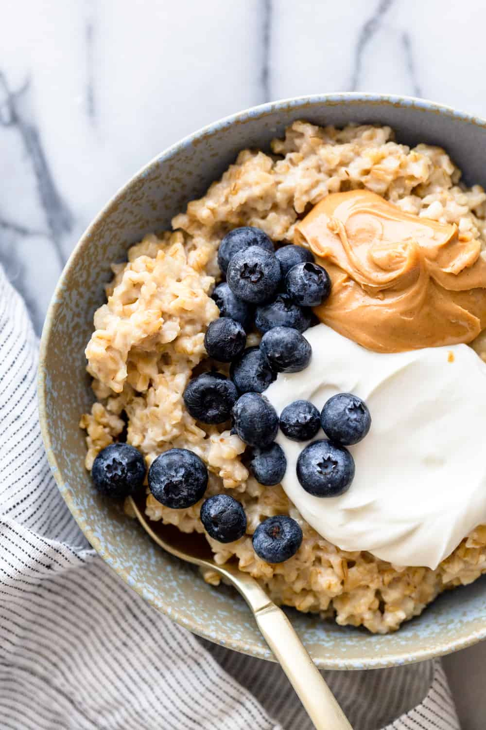 steel cut oatmeal with blueberries, peanut butter and yogurt. In a blue bowl with a spoon.