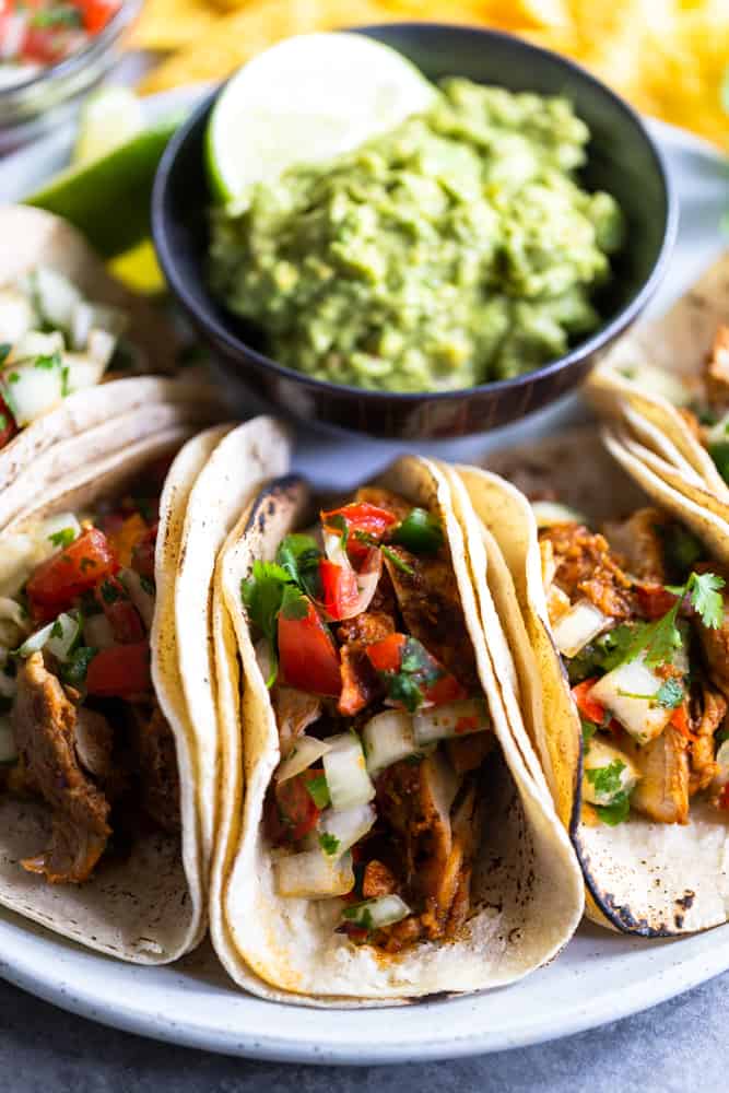 Chili lime chicken tacos on a white plate with a small dish of guacamole