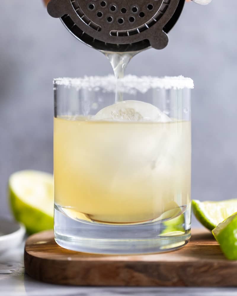 margarita being poured from a cocktail shaker into a glass over ice.