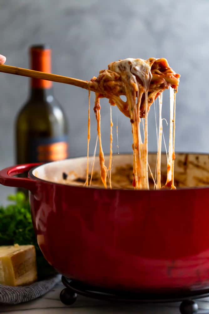 Cheesy lasagna being served from a red dutch oven