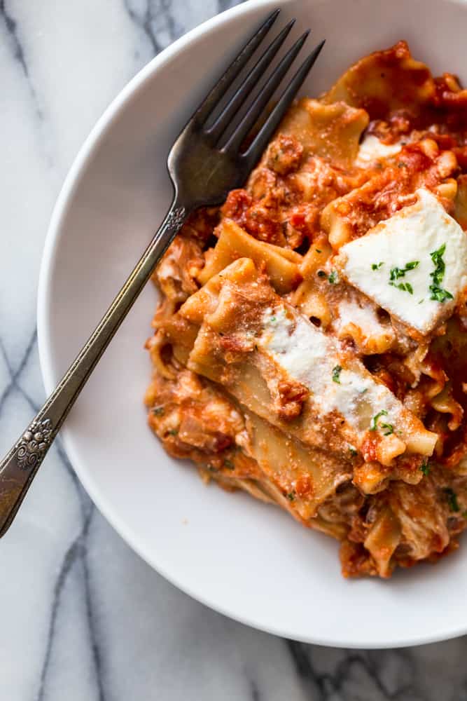 White bowl on marble background with lasagna and a fork