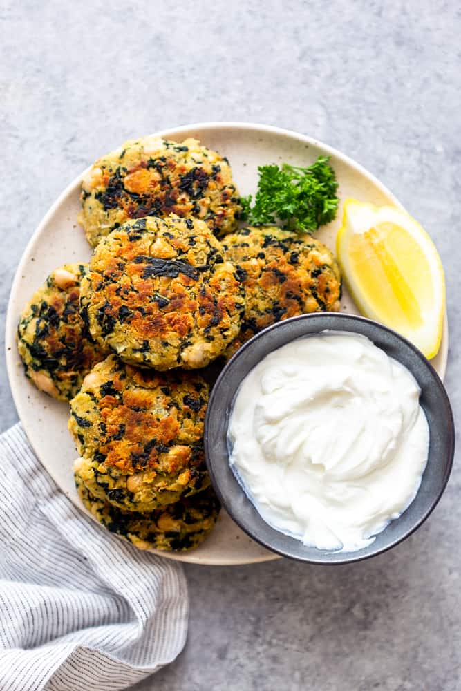 white bean kale patties on a white place with a small bowl of yogurt and lemon slice