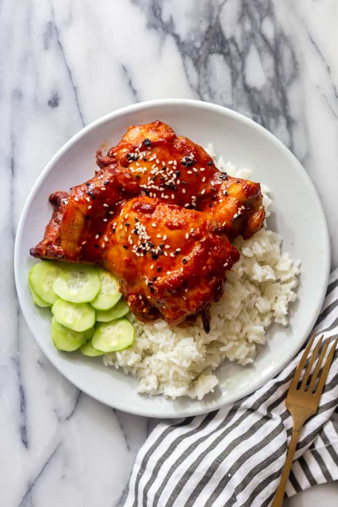 Sticky Korean Thighs on a white plate with white rice and sliced cucumbers.