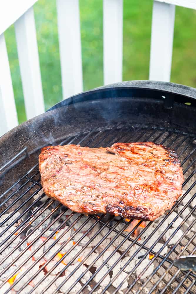 Flank steak being cooked on a charcoal grill outdoors