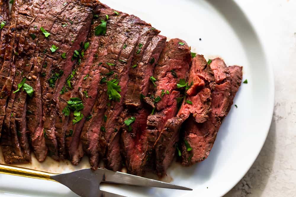 Sliced grilled flank steak on a white platter