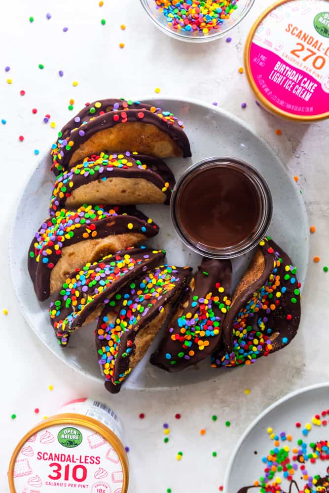 Ice cream tacos with chocolate coating and bright sprinkles on a white plate.