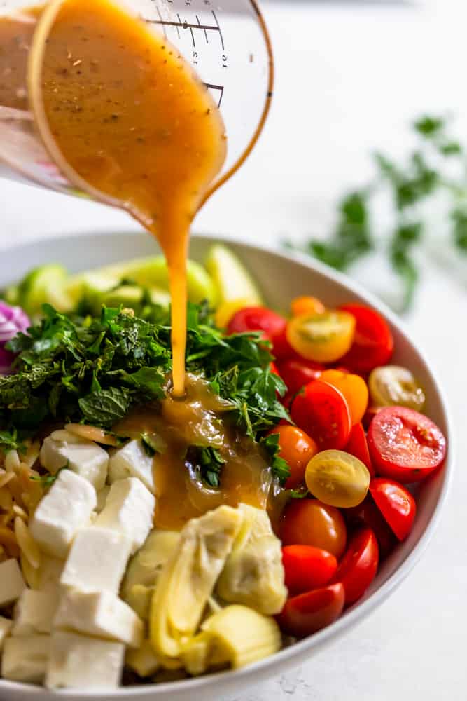 Lemon dressing pouring onto orzo salad