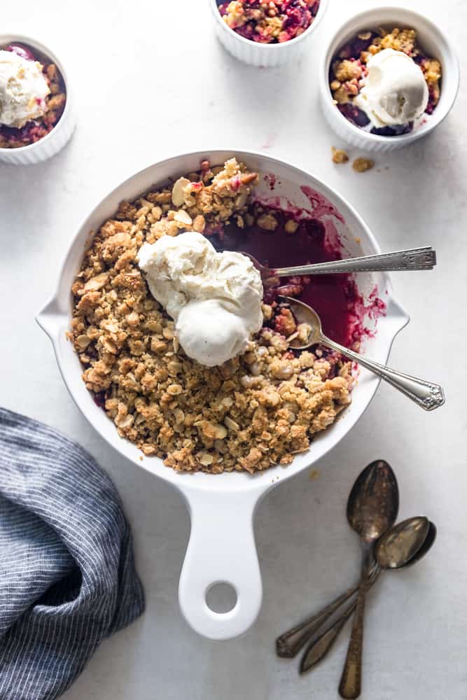 Cherry almond crisp in a white baking dish with 3 scoops of vanilla ice cream and two spoons