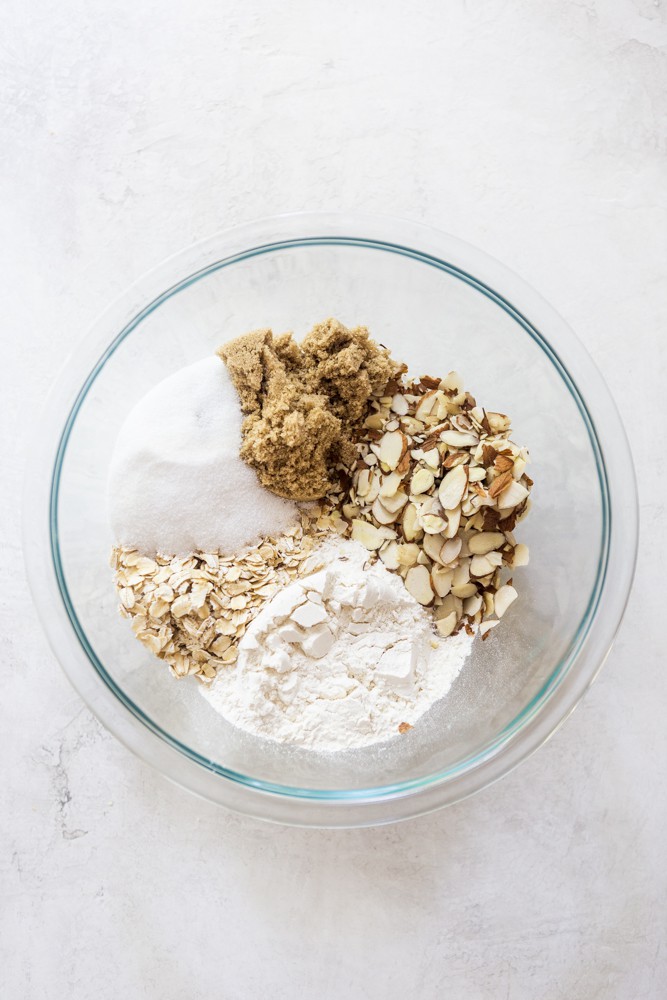ingredients for crisp topping - flour, oats, brown sugar, white sugar, sliced almonds - in a glass bowl
