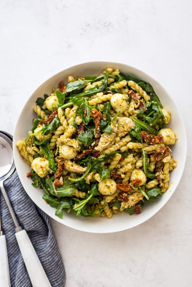 Chicken Pesto Pasta Salad in a white bowl with blue striped dishtowel and serving spoon