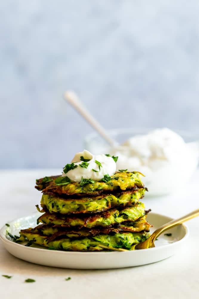 Stack of zucchini fritters on a white place with garlic yogurt sauce.