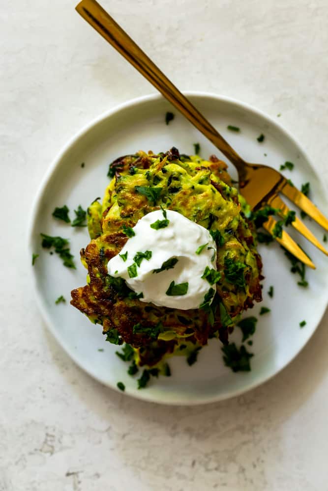 Zucchini fritters on a white plate with a gold fork, topped with garlic yogurt sauce