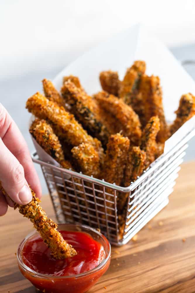 Basket of zucchini fries, one being dipped into ketchup