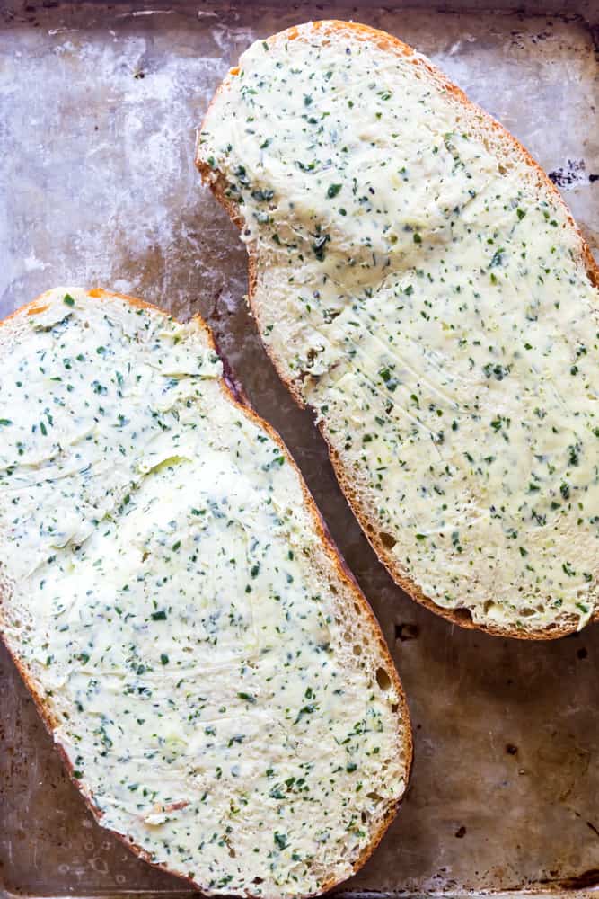 Loaf of bread cut in half with garlic butter spread on top.