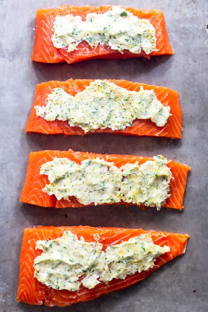 Raw salmon on baking sheet with garlic butter spread on top, about to go in the oven
