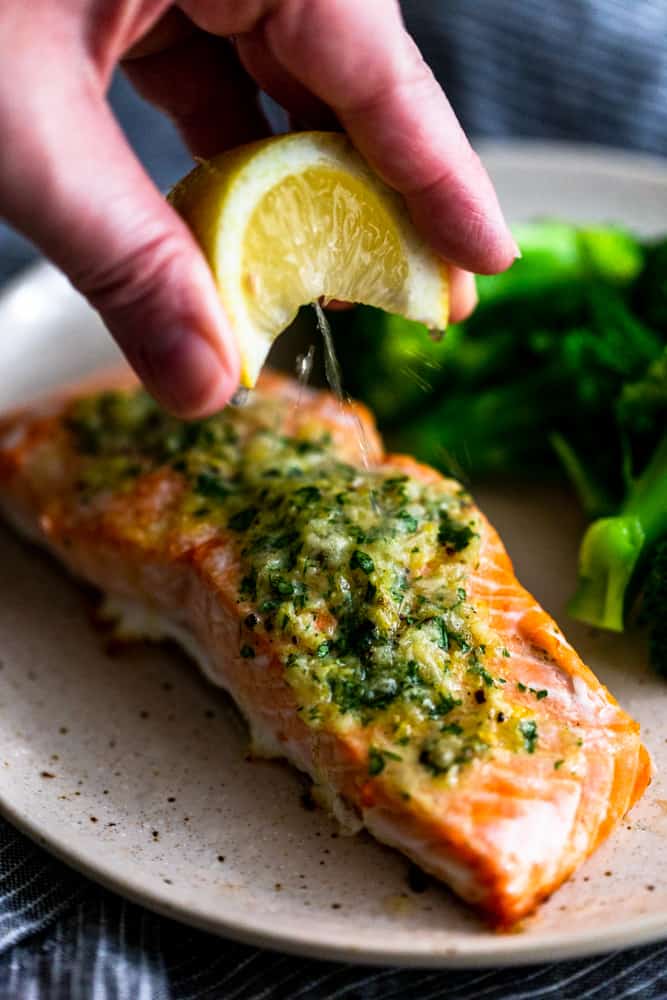 Lemon wedge being squeezed over salmon