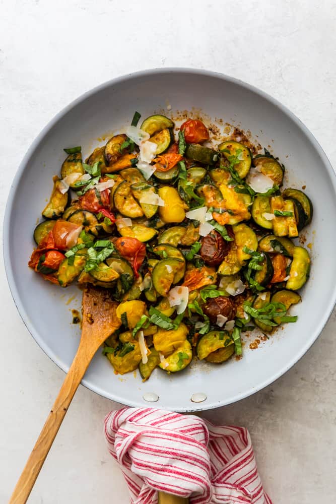 Sauteed zucchini and cherry tomatoes in a pan with a wooden spoon