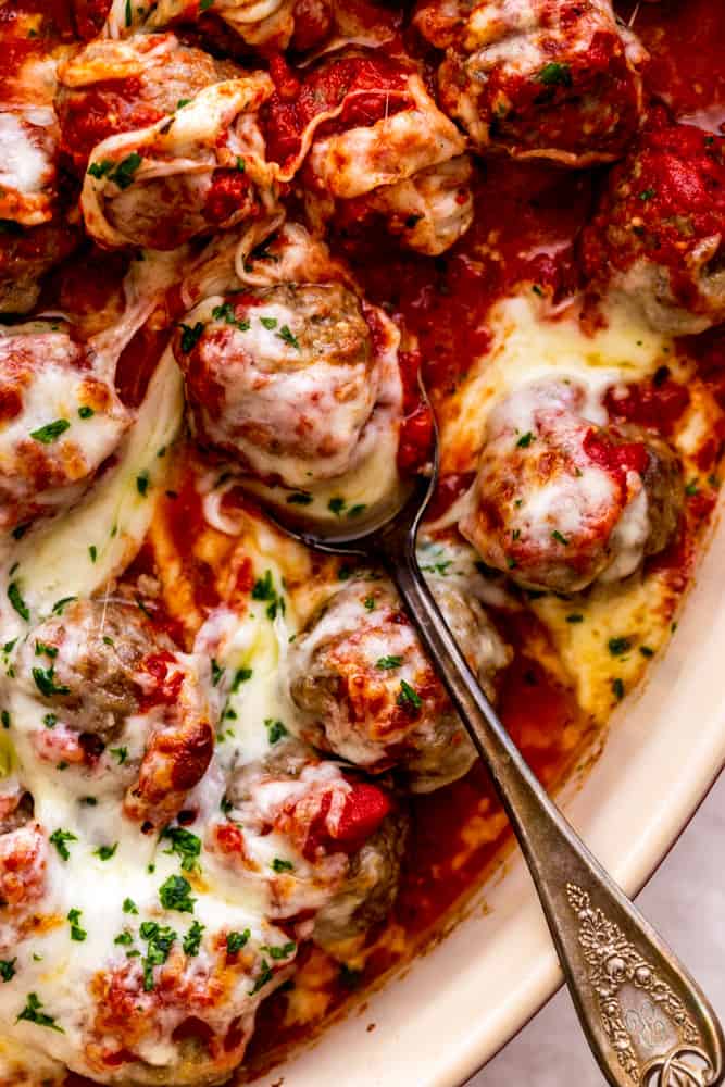 Cheesy meatballs in a dish, one is in a spoon.