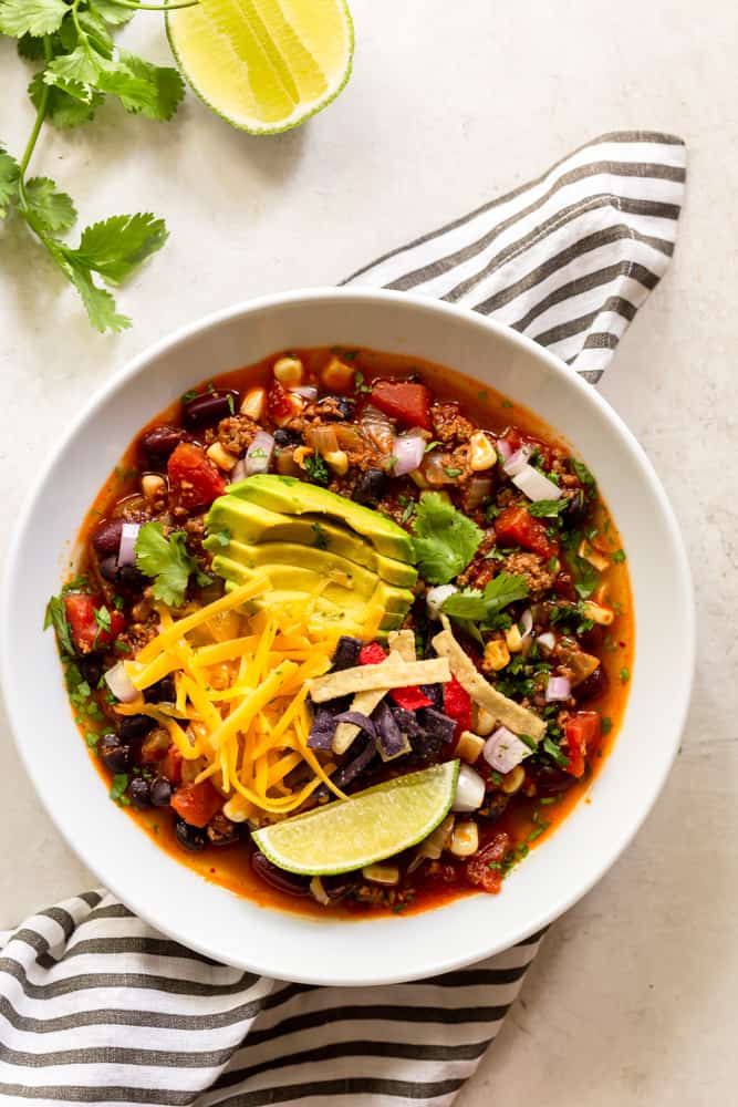 Taco Soup garnished with shredded cheese, avocado, tortilla strips, cilantro and lime. 