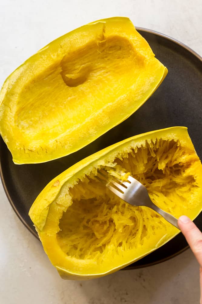 A spaghetti squash cut in half after being cooked, showing a fork shredding it into "noodles"