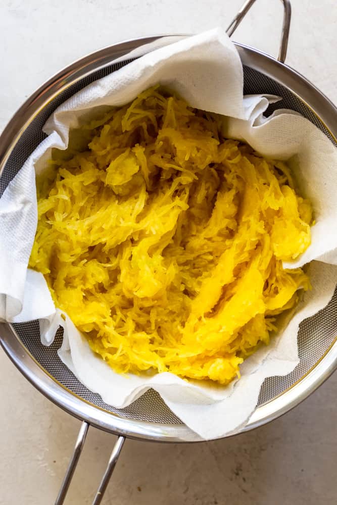 cooked spaghetti squash draining in a colander lines with paper towels