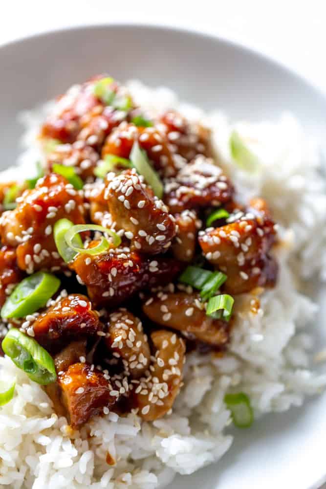 Close up of sesame chicken with sesame seeds and green onions over a bed of rice