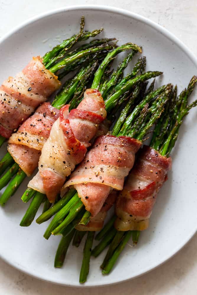 Asparagus bundles wrapped in bacon on a white plate