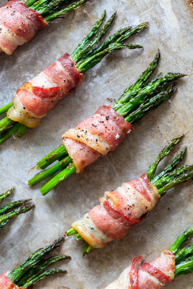 Bacon wrapped asparagus bundles on a baking sheet