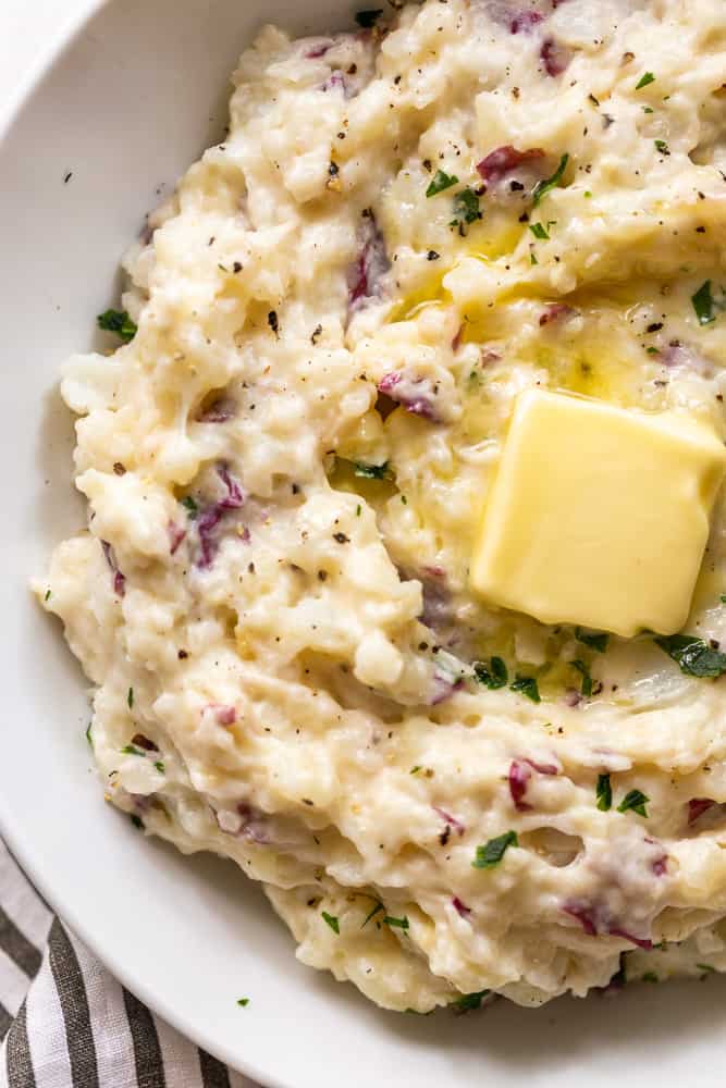 Closeup of garlic mashed potatoes in a white bowl with butter on top
