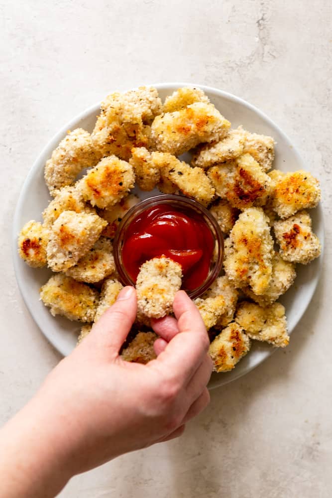 Hand dipping a baked chicken nugget into ketchup